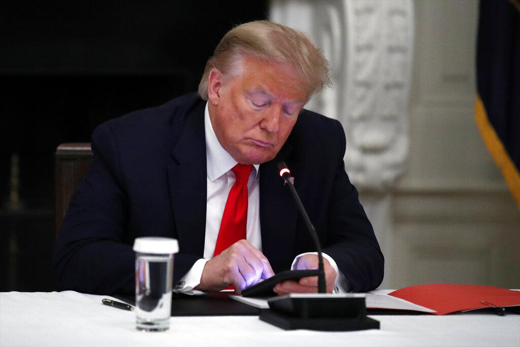 In this Thursday, June 18, 2020 file photo, President Donald Trump looks at his phone during a roundtable with governors on the reopening of America’s small businesses, in the State Dining Room of the White House in Washington. (AP Photo / Alex Brandon, File)