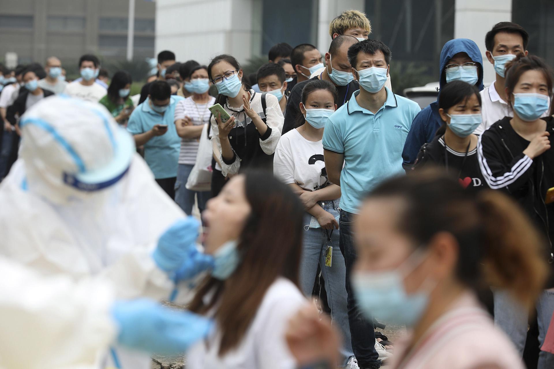 In this Friday, May 15, 2020 file photo, people line up for coronavirus testing at a large factory in Wuhan in central China's Hubei province. In June 2020, China reported using batch testing as part of a recent campaign to test all 11 million residents of Wuhan, the city where the virus first emerged late in late 2019. (Chinatopix Via AP)
