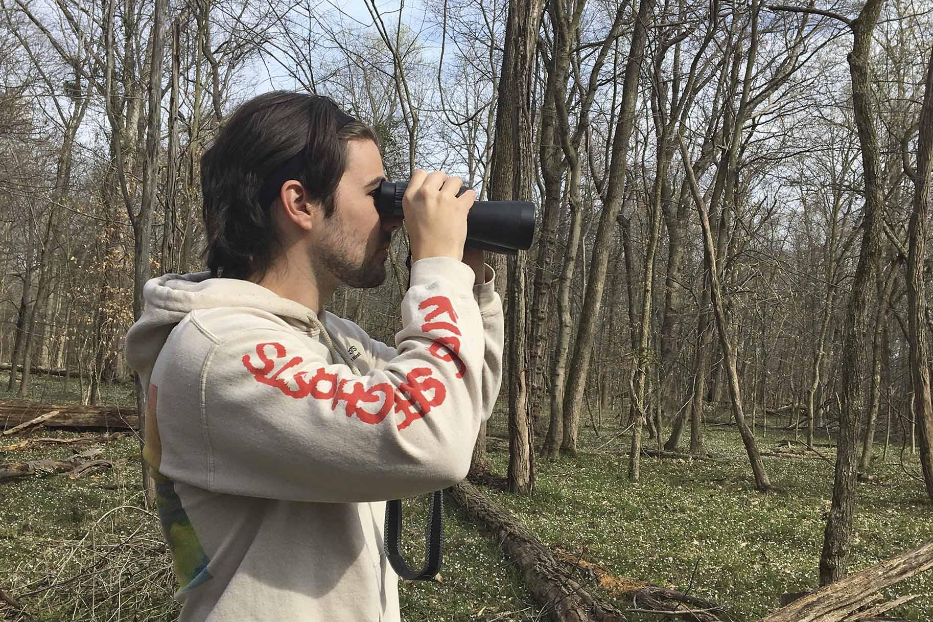 In this March 24, 2020 photo, provided by Conner Brown, he is seen using binoculars to look for birds in Cedar Island, Maryland. (Elizabeth Wright / Courtesy of Conner Brown via AP)
