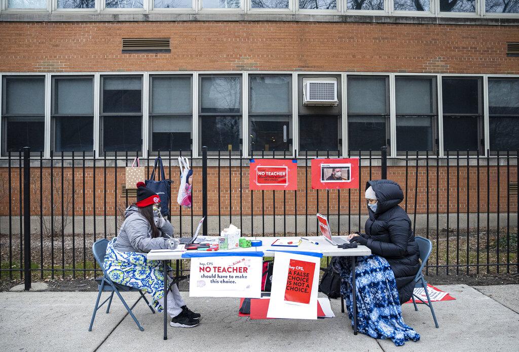 In this Monday, Jan. 11, 2021 file photo, teachers Adrienne Thomas, left, and Irene Barrera, right set up their computers and materials for their virtual classes outside of Suder Montessori Magnet Elementary School in solidarity with pre-K educators forced back into the building in Chicago. (Anthony Vazquez / Chicago Sun-Times via AP, File)