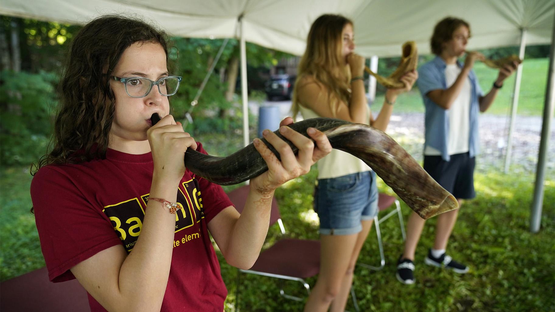 Robin Asch, left, Ava Katz, center, and Noah Katz practice playing their shofars, the ancient musical horns used in Judaism, under a tent set upon outside Temple Beth El, Monday, Aug. 30, 2021, in Augusta, Maine. (AP Photo / Robert F. Bukaty)