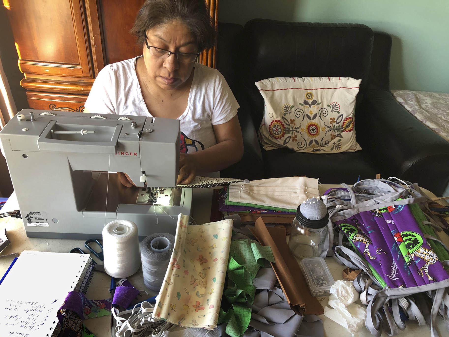 In this April 7, 2020, photo provided by Maribel Torres, Maribel Torres sews face masks masks to be used for protection against the coronavirus at her home in the Staten Island borough of New York. (Pablo Evangelista / Torres Family Photo via AP)