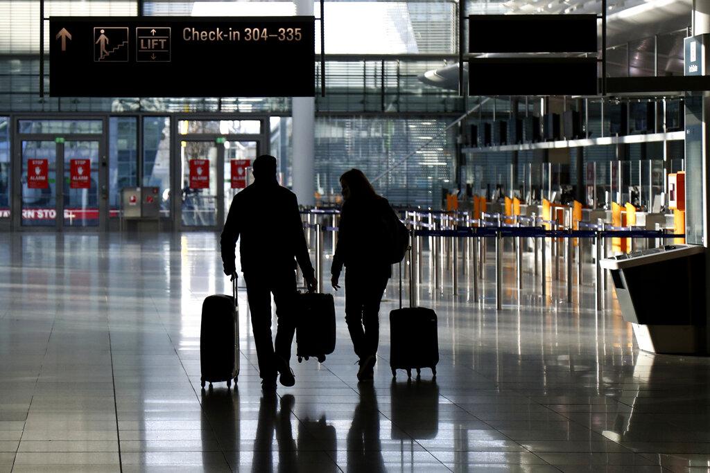 In this Saturday, Dec. 26, 2020 file photo, people walk with their luggage through a deserted check-in hall at the airport in Munich, Germany as Germany continues its second lockdown to avoid the further outspread of the coronavirus. (AP Photo / Matthias Schrader)