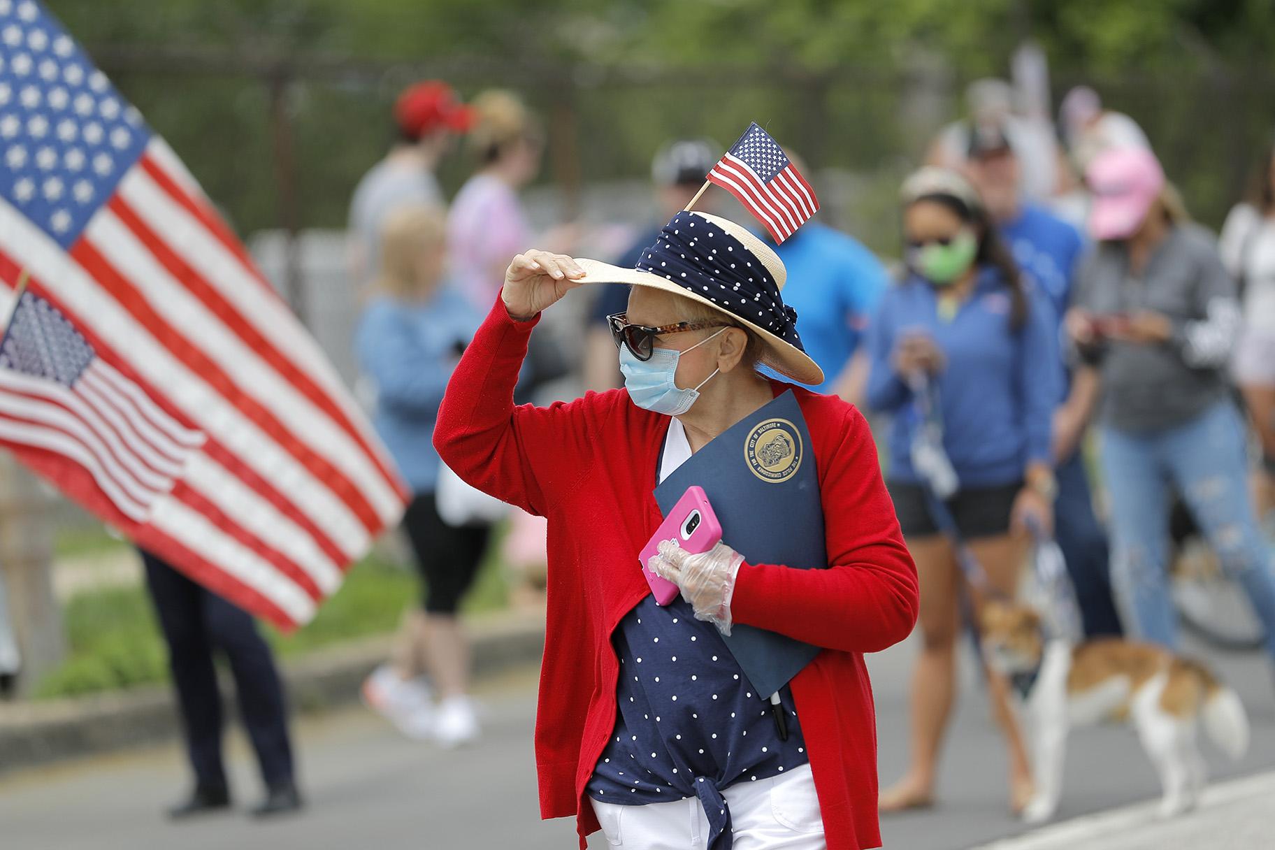 A woman holds on to her hat as she gathers with people outside of Fort McHenry National Monument and Historic Shrine, where President Donald Trump attends a Memorial Day ceremony, Monday, May 25, 2020, in Baltimore. (AP Photo / Julio Cortez)