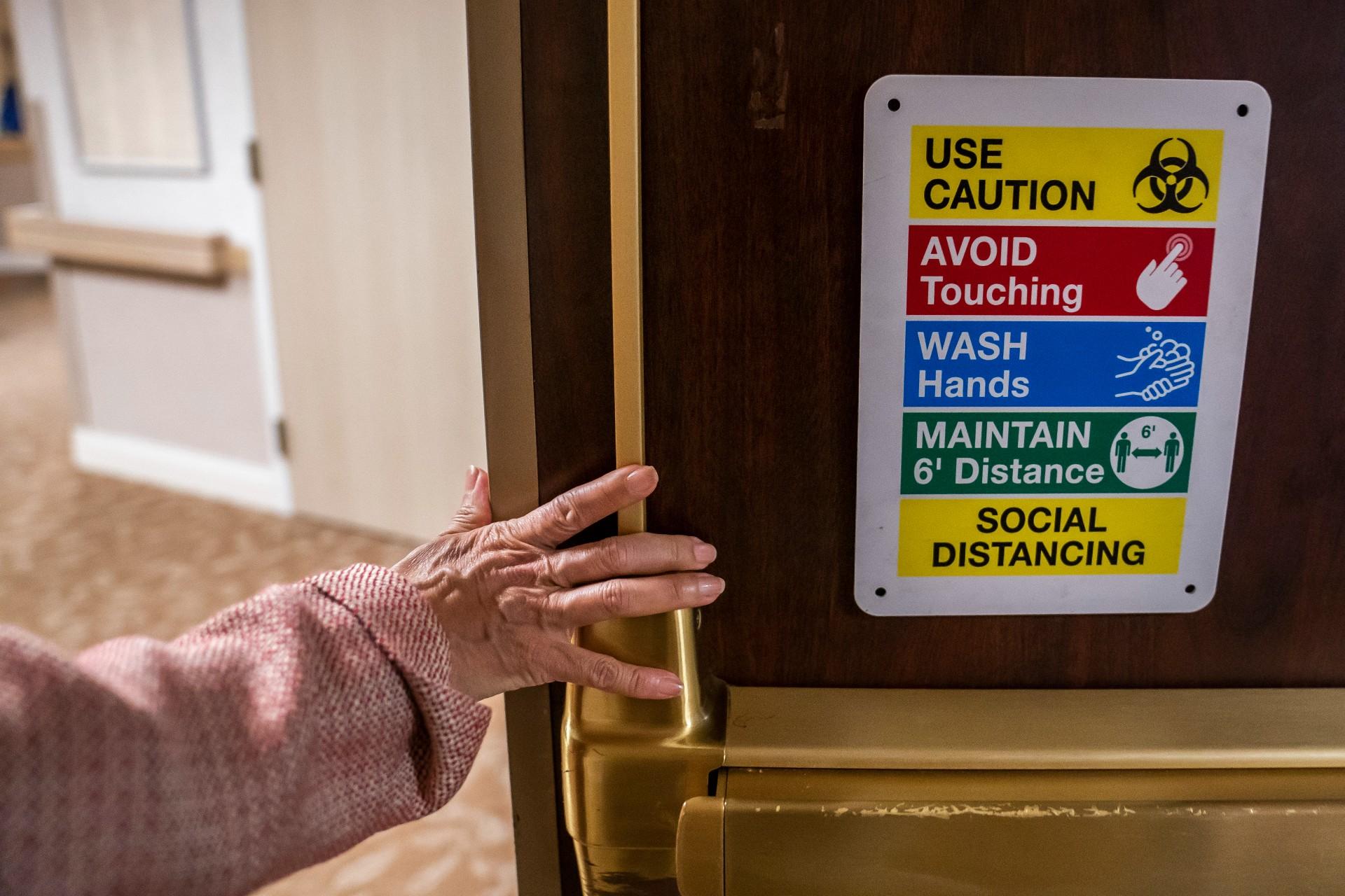 Tina Sandri, CEO of Forest Hills of DC senior living facility, passes a COVID-19 informational sign while walking to her office on Thursday, Dec. 8, 2022, in Washington. Coronavirus-related hospital admissions are climbing again in the United States, with older adults a growing share of U.S. deaths. (AP Photo / Nathan Howard)