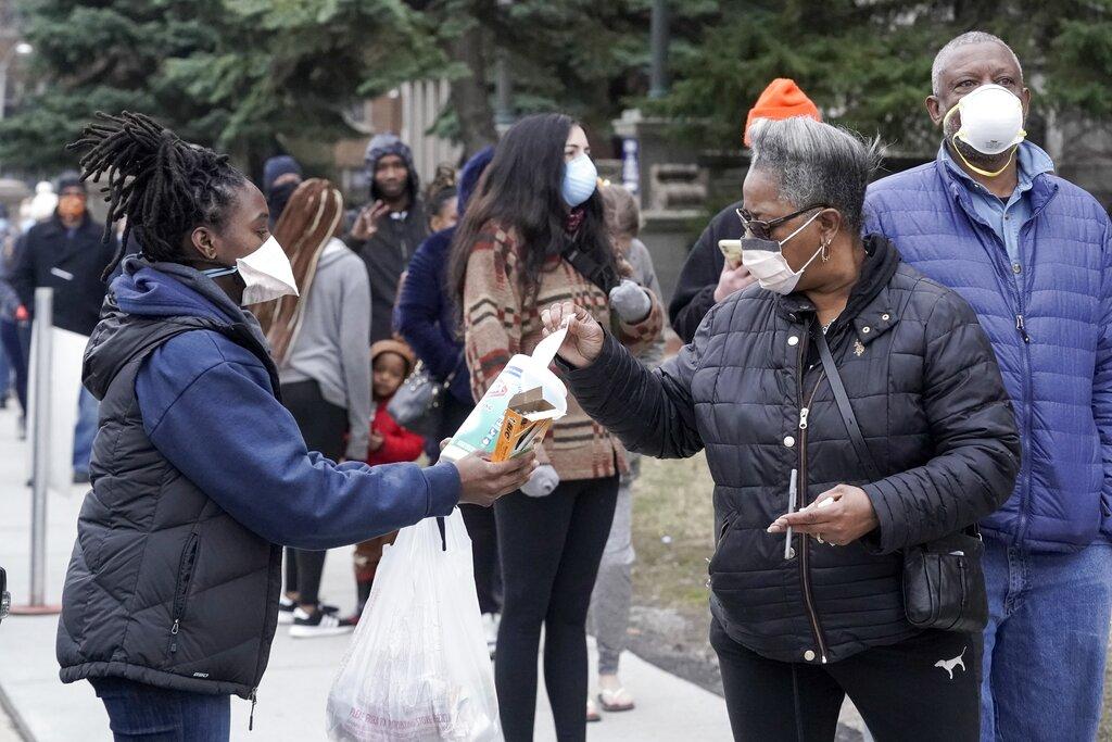 A worker hands out disinfectant wipes and pens as voters line up outside Riverside High School for Wisconsin's primary election Tuesday April 7, 2020, in Milwaukee. (AP Photo / Morry Gash