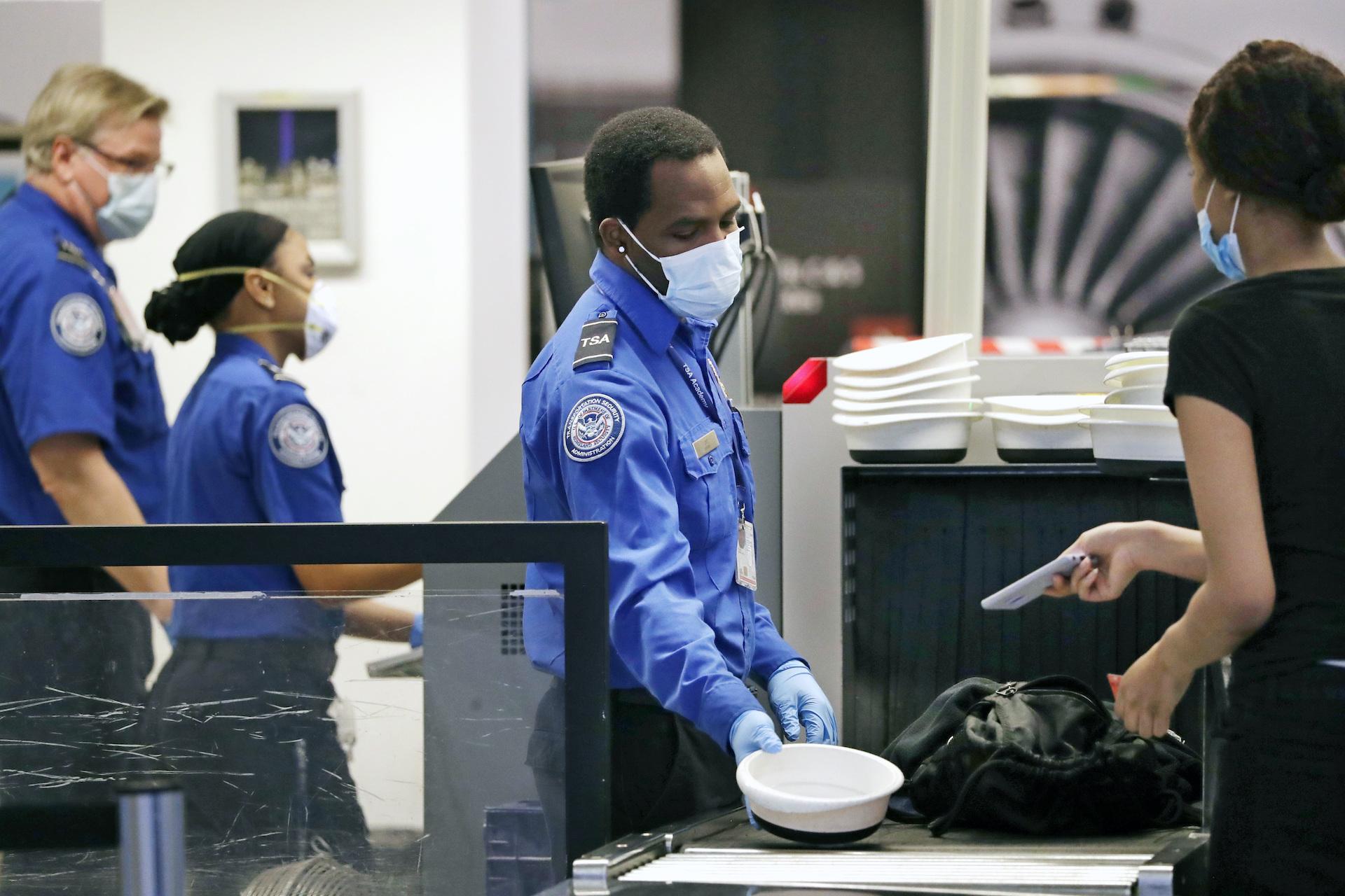 TSA officers wear protective masks at a security screening area at Seattle-Tacoma International Airport Monday, May 18, 2020, in SeaTac, Wash. (AP Photo/Elaine Thompson)