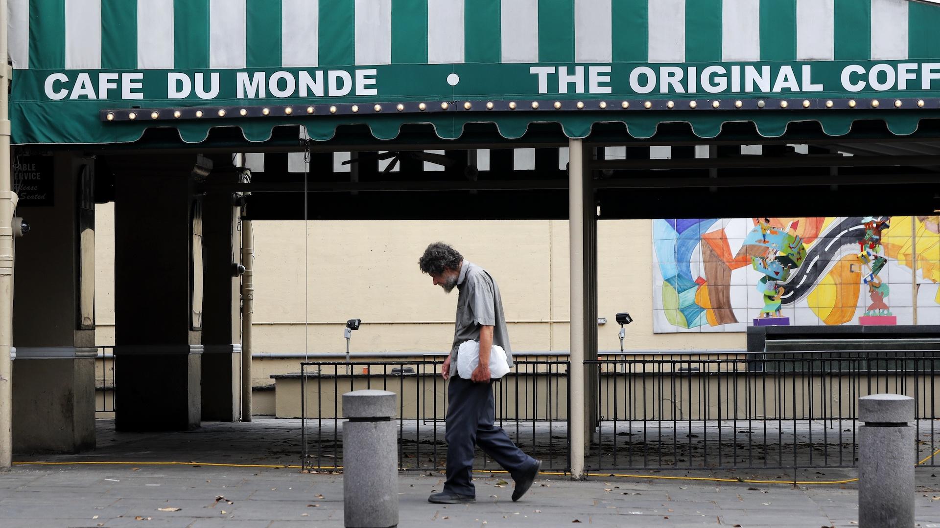In this March 27, 2020, file photo, a man walks past the Cafe Du Monde restaurant, which was closed but has since reopened, in the French Quarter of New Orleans. (AP Photo/Gerald Herbert, File)