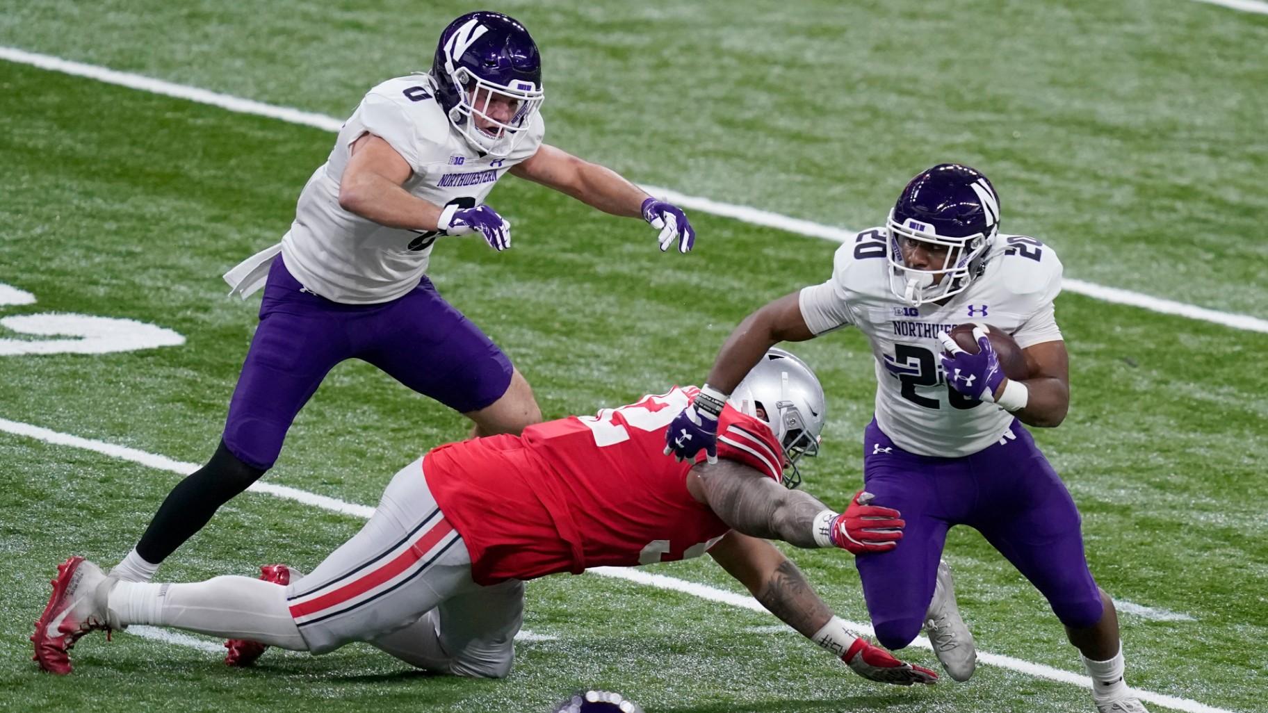 Northwestern running back Cam Porter (20) runs with the ball as Ohio State defensive tackle Haskell Garrett defends and teammate John Raine (0) watches during the first half of the Big Ten championship NCAA college football game, Saturday, Dec. 19, 2020, in Indianapolis. (AP Photo / Darron Cummings, File)