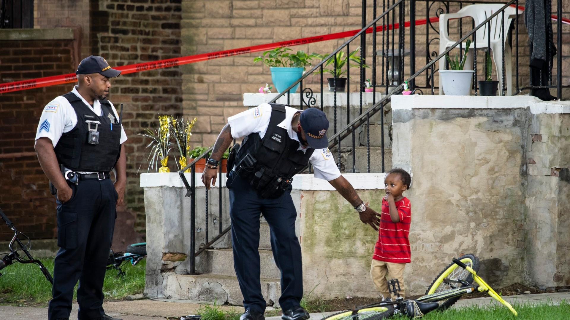 A Chicago police officer helps a child walk through an area being investigated after two men were shot Friday, July 3, 2020, in Chicago. (Ashlee Rezin Garcia / Chicago Sun-Times via AP)
