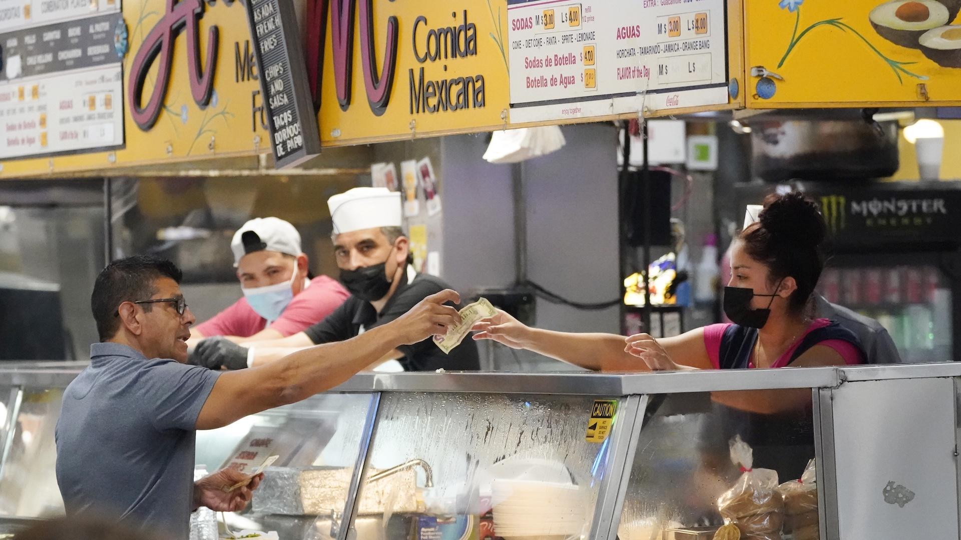 Money is exchanged at a food stand while workers wear face masks inside Grand Central Market on Wednesday, July 13, 2022, in Los Angeles. (AP Photo/Marcio Jose Sanchez)