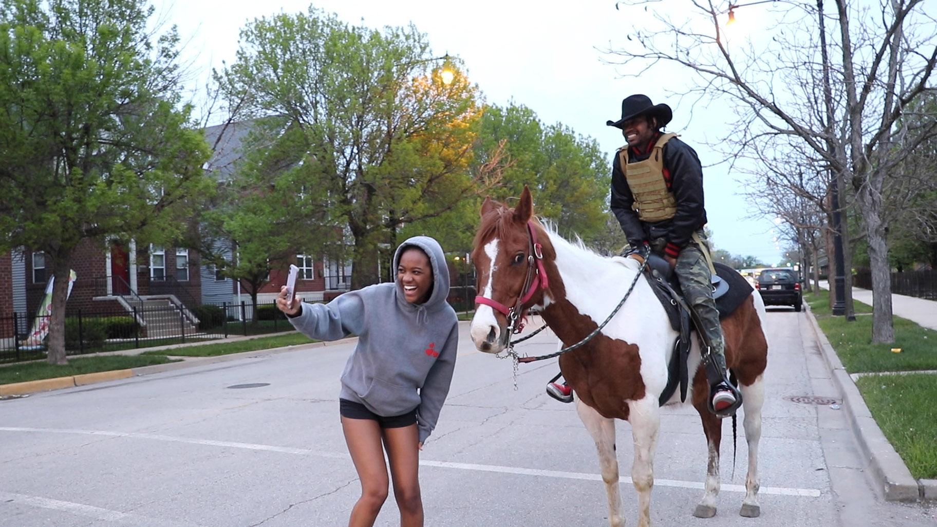 A young woman takes a photo with Adam Hollingsworth, also known as the Dreadhead Cowboy, and his 13-year-old horse Prince in the Woodlawn neighborhood on Chicago’s South Side on Saturday, May 16. (Evan Garcia / WTTW News)