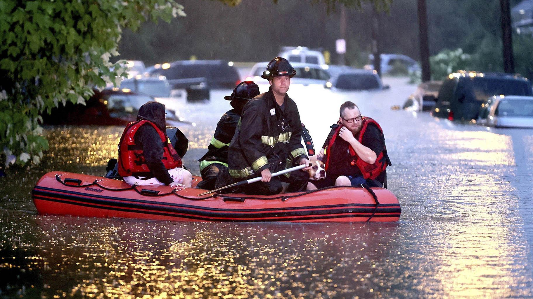 Steven Bertke and his dog Roscoe are taken to dry land by St. Louis firefighters who used a boat to rescue people from their flooded homes on Hermitage Avenue in St. Louis on Tuesday, July 26, 2022. (David Carson / St. Louis Post-Dispatch via AP)