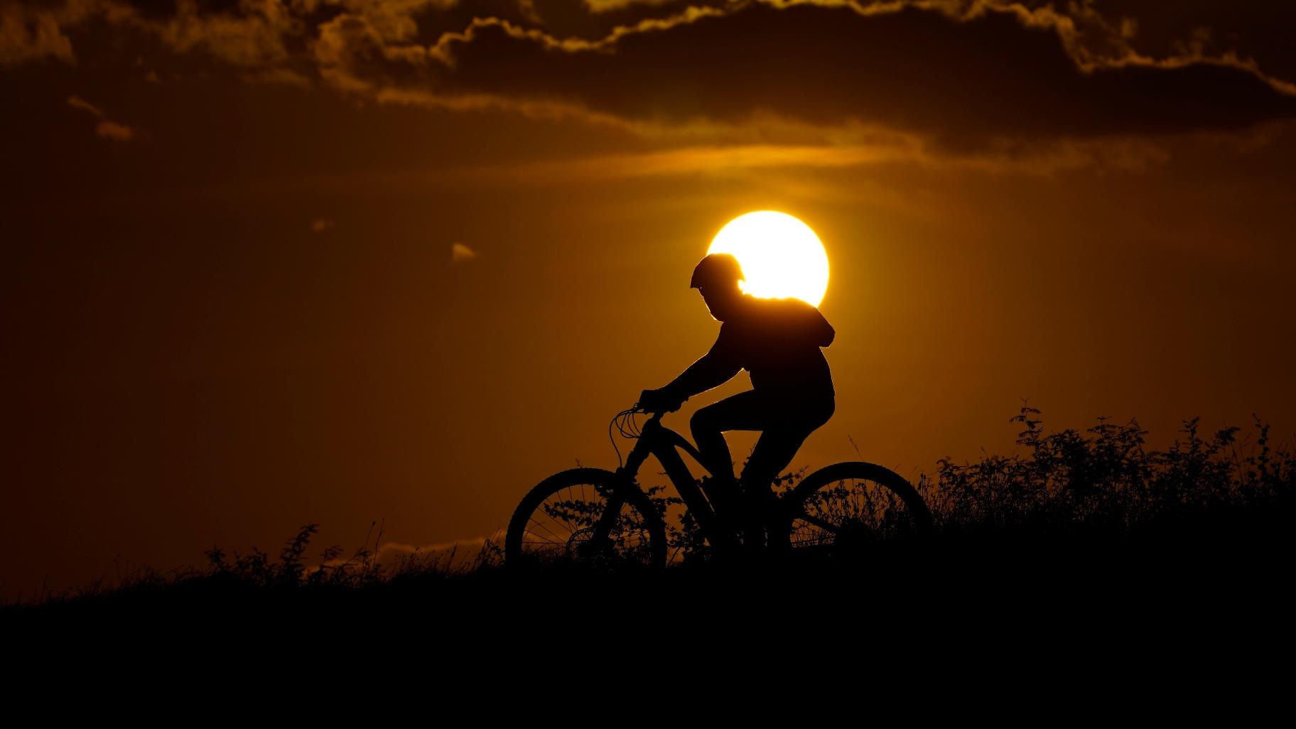 A cyclist tops a hill on a hot day at sunset, Aug. 20, 2023, in San Antonio. (AP Photo / Eric Gay, File)