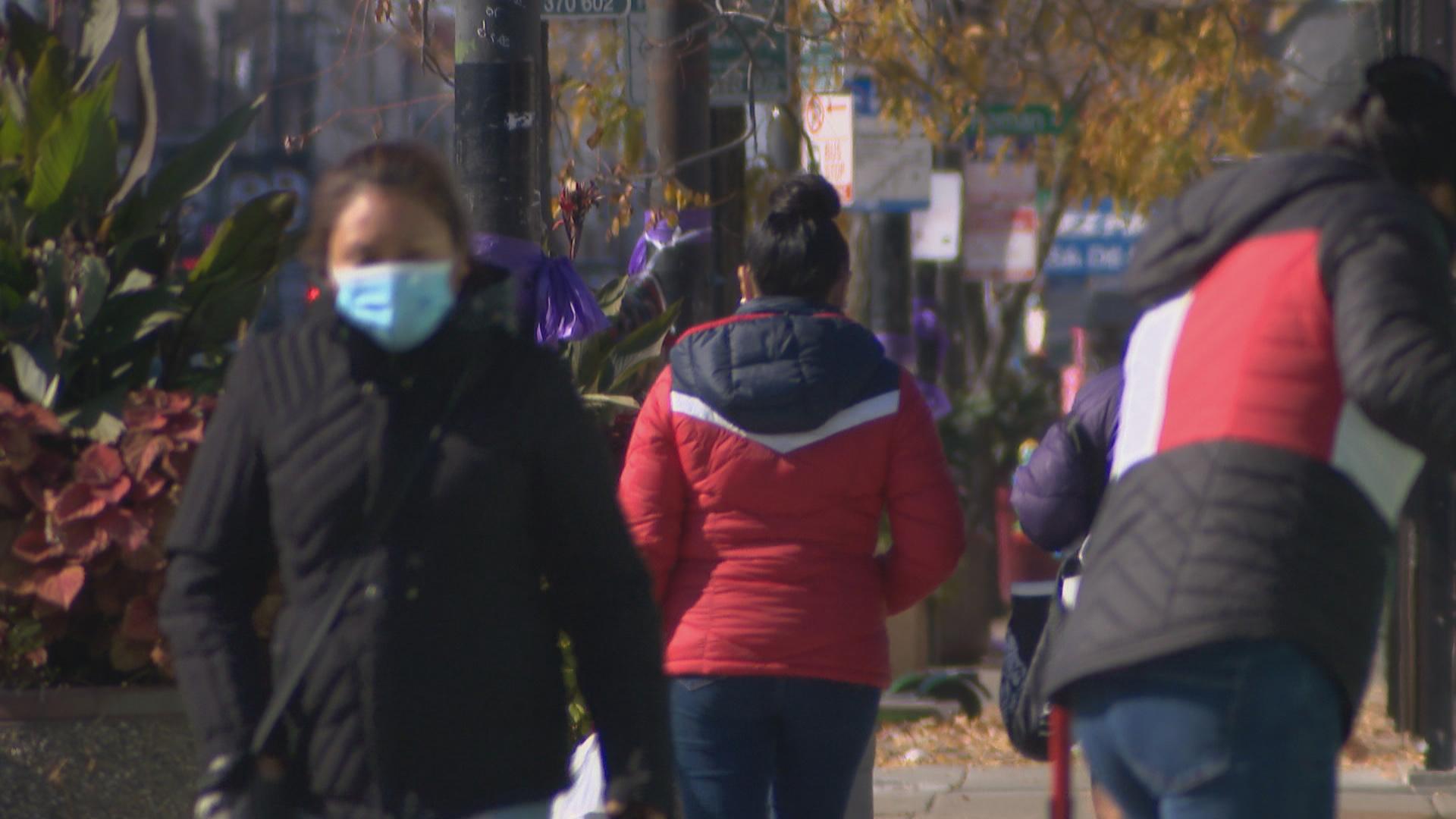 People wearing masks walk along the street in Little Village. (WTTW News)