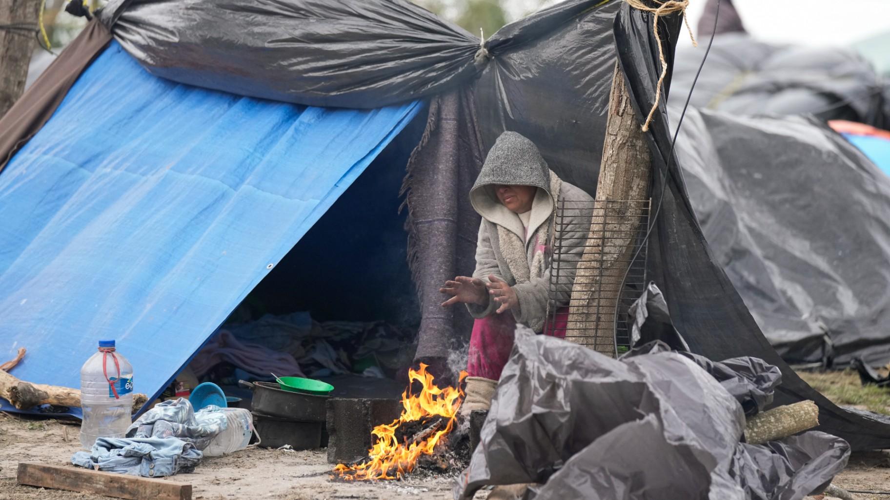 A Venezuelan migrant warms her hands over a campfire outside her makeshift tent refusing to be relocated to a refugee shelter, in Matamoros, Mexico, Friday, Dec. 23, 2022. (AP Photo / Fernando Llano)