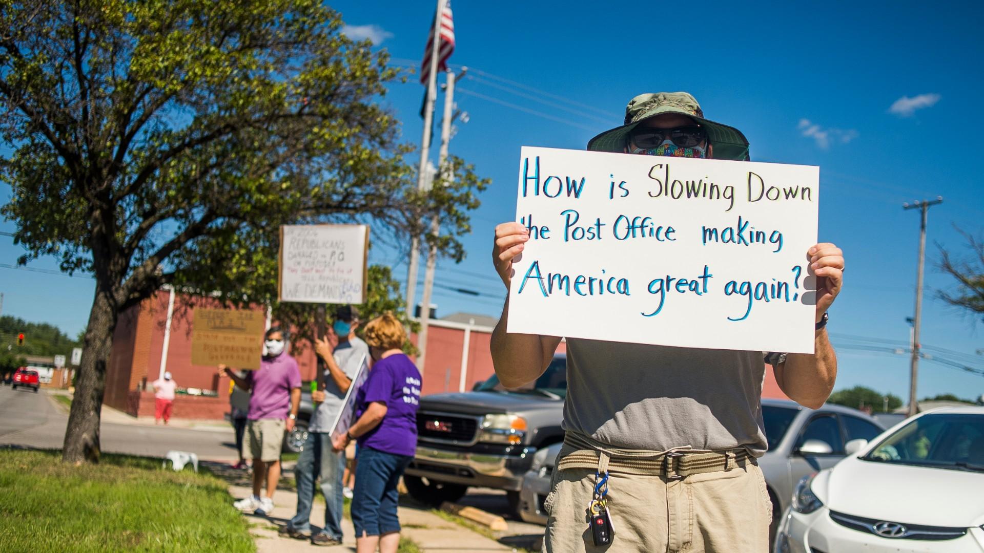 Eric Severson holds a sign as a few dozen people gather in front of the United States Post Office on Rodd St. to protest recent changes to the U.S. Postal Service under new Postmaster General Louis DeJoy on Tuesday, Aug. 11, 2020 in Midland, Mich. (Katy Kildee / Midland Daily News via AP)