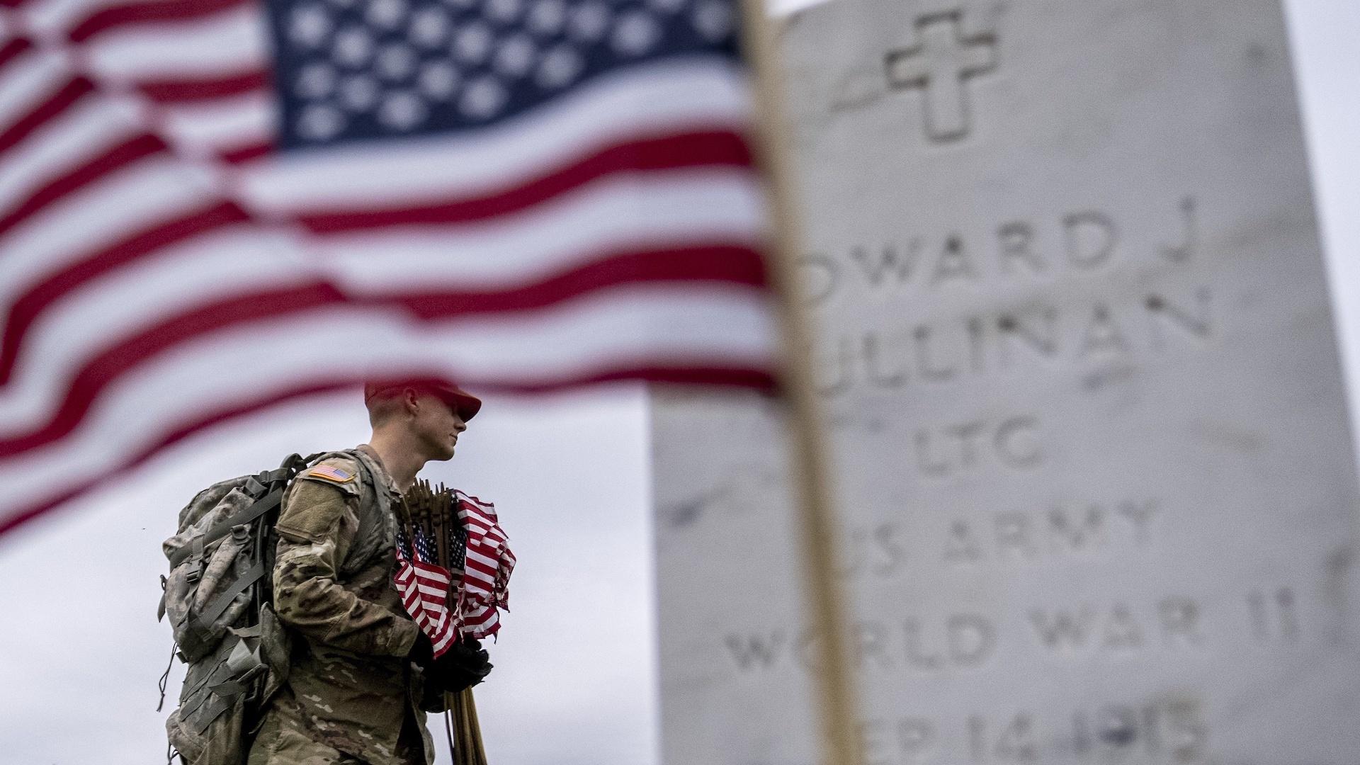 A member of the 3rd U.S. Infantry Regiment, also known as The Old Guard, places flags in front of each headstone for "Flags-In" at Arlington National Cemetery in Arlington, Thursday, May 25, 2023, to honor the Nation's fallen military heroes ahead of Memorial Day. (AP Photo/Andrew Harnik)