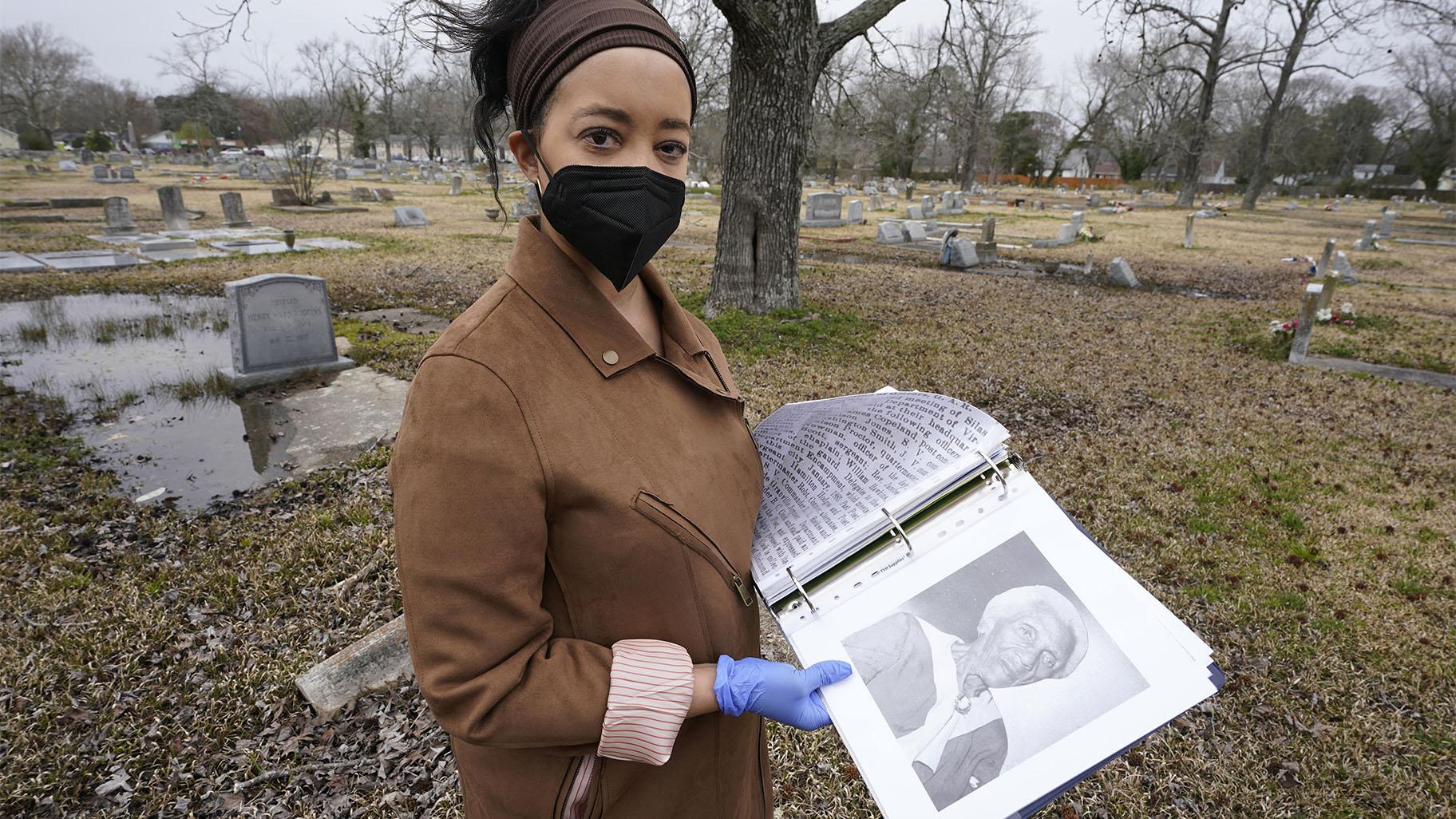 Nadia Orton, a genealogist and family historian in Virginia, opens a binder of research next to the grave of a Civil War era slave at the Lincoln Memorial Cemetery in Portsmouth, Va., Tuesday, March 23, 2021. Orton has worked tracing her own family and others to historically Black cemeteries. (AP Photo / Steve Helber)
