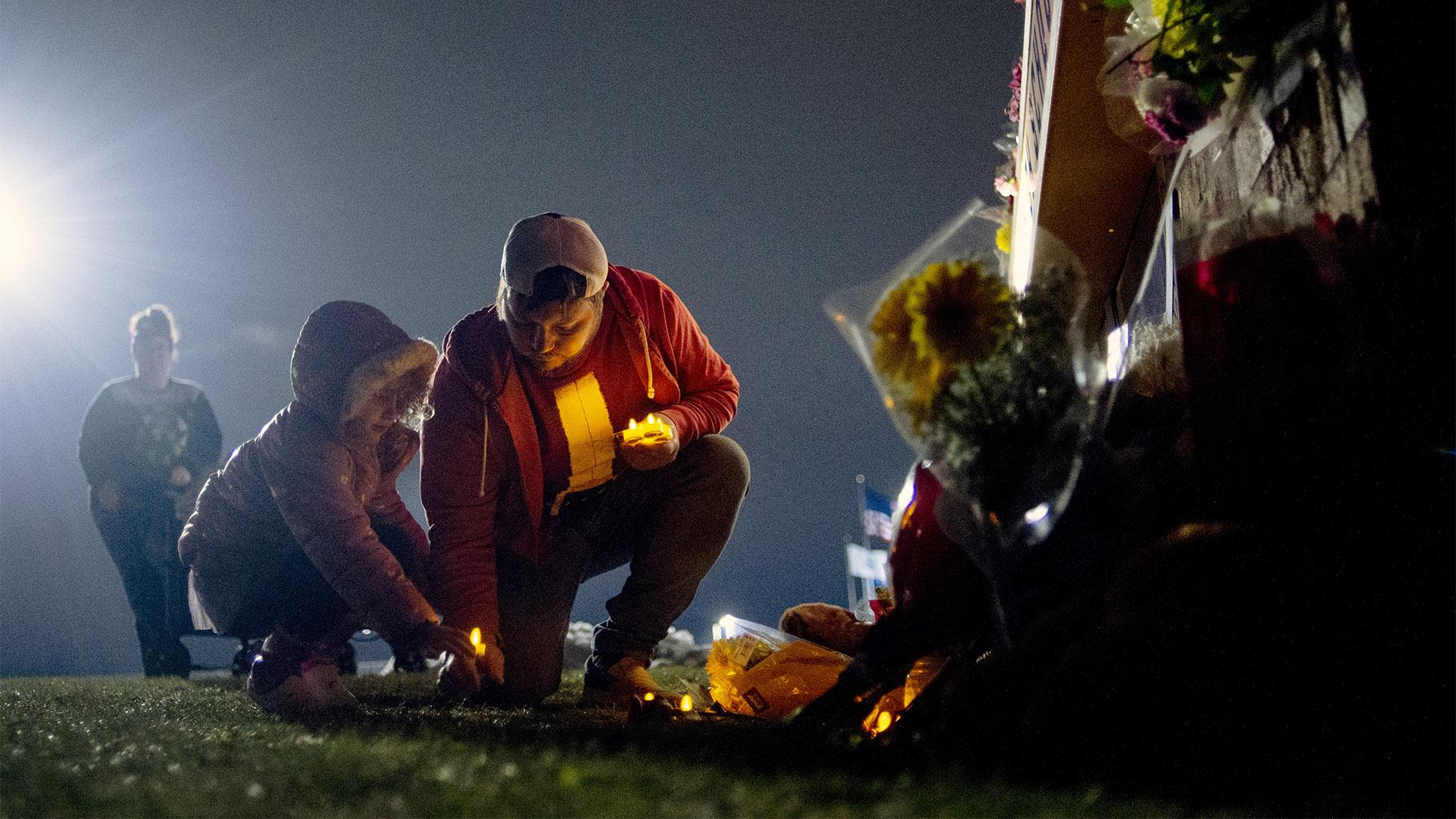 Waterford resident Andrew Baldwin, cousin of Madisyn Baldwin, places candles at the base of a a memorial with his 5-year-old daughter Ariyah Baldwin on Wednesday, Dec. 1, 2021 outside of Oxford High School in Oxford, Mich.  (Jake May / The Flint Journal via AP)