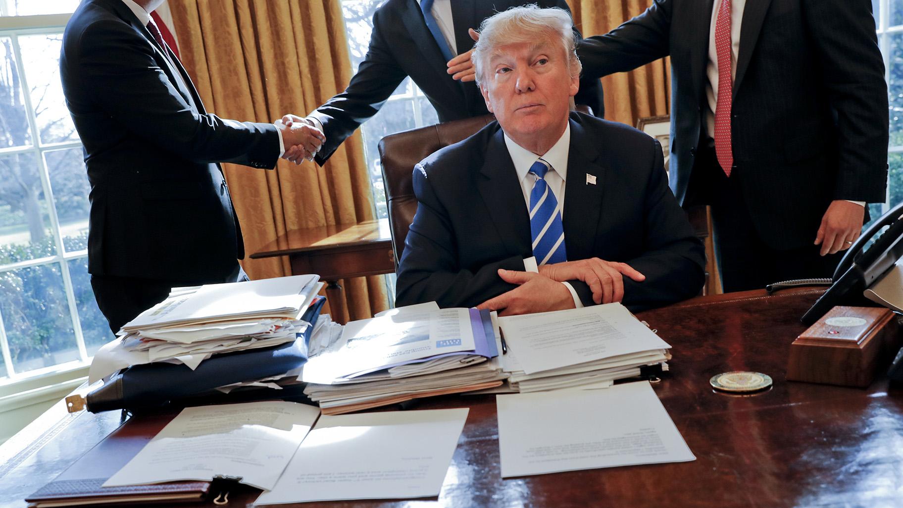 President Donald Trump sits at his desk after a meeting with Intel CEO Brian Krzanich, left, and members of his staff in the Oval Office of the White House in Washington, Feb. 8, 2017, as a lockbag is visible on the desk, the key still inside at left. (AP Photo / Pablo Martinez Monsivais, File)