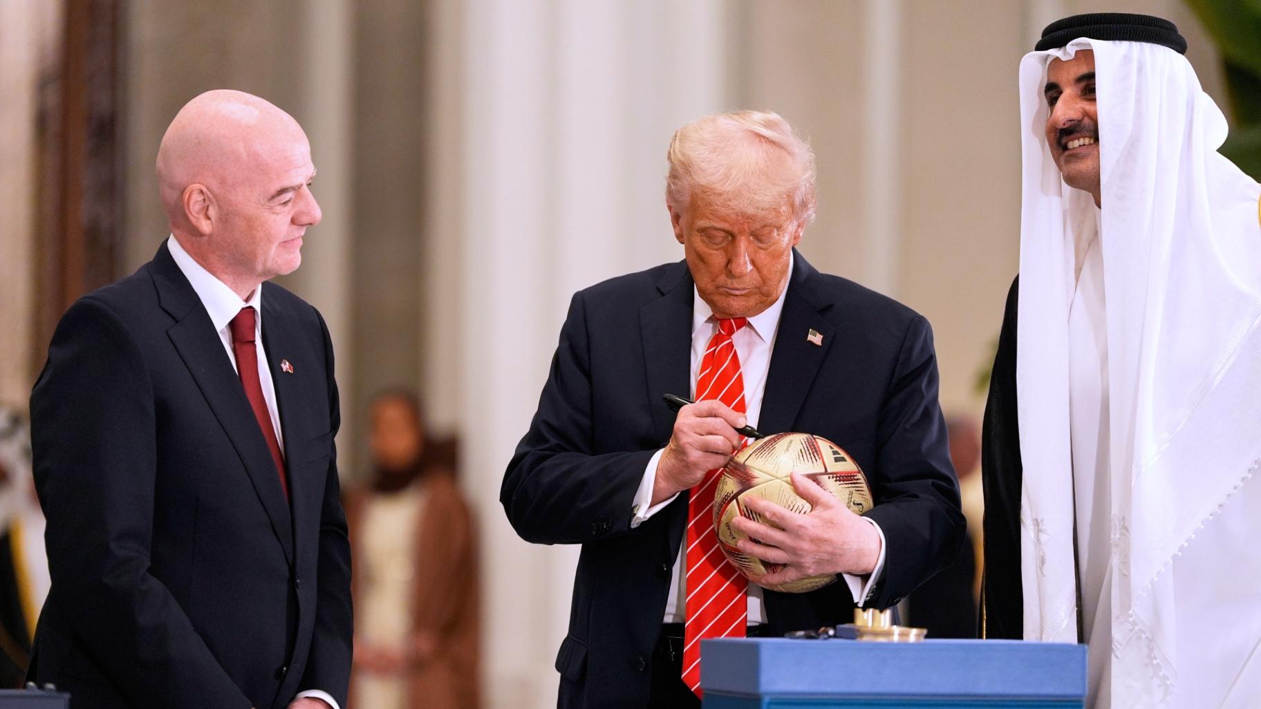 President Donald Trump signs a FIFA soccer ball as Qatar's Emir Sheikh Tamim bin Hamad Al Thani and FIFA President Gianni Infantino looks on at the Lusail Palace, Wednesday, May 14, 2025, in Doha, Qatar, as they marked the passing of World Cup hosting duties from Qatar, which held it in 2022, to the United States, which is hosting in 2026. (AP Photo / Alex Brandon)