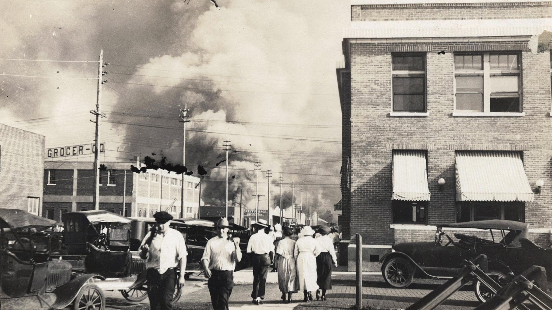 In this photo provided by Department of Special Collections, McFarlin Library, The University of Tulsa, two armed men walk away from burning buildings as others walk in the opposite direction during the June 1, 1921, Tulsa Race Massacre in Tulsa, Okla. (Department of Special Collections, McFarlin Library, The University of Tulsa via AP, File)