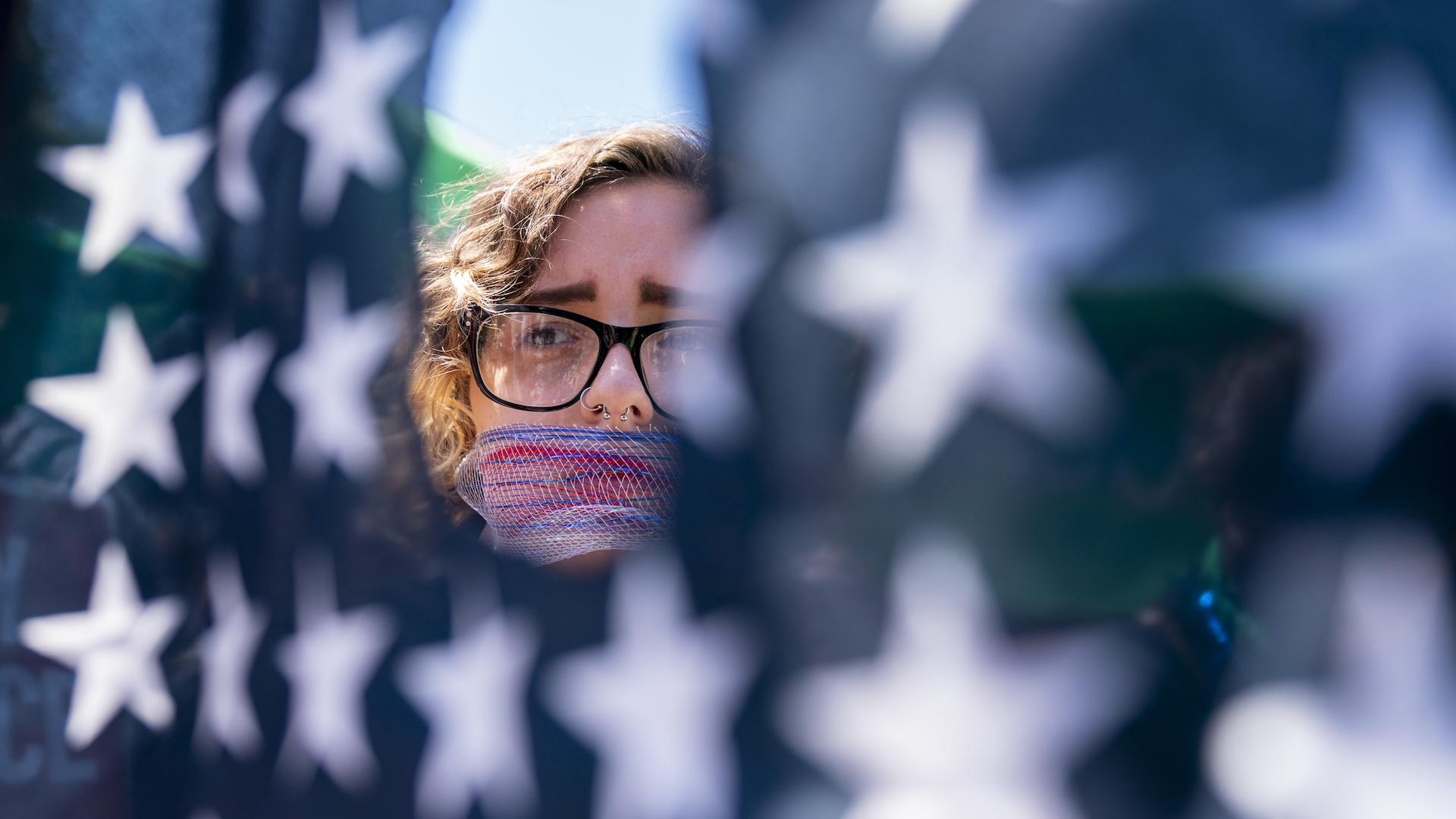 Emma Rousseau of Oakland, N.J., her mouth bound with a red, white and blue netting, attends a rally on the Fourth of July to protest for abortion rights, at Lafayette Park in front of the White House in Washington, Monday, July 4, 2022. (AP Photo/Andrew Harnik, File)
