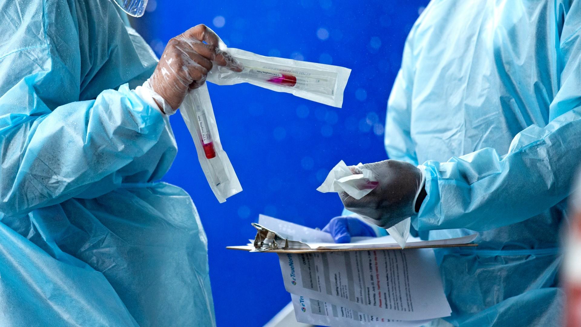 In this July 23, 2020 file photo, health care workers prepare a COVID-19 test sample before a person self-administered a test at the COVID-19 drive-thru testing center at Miami-Dade County Auditorium in Miami. (David Santiago / Miami Herald via AP)