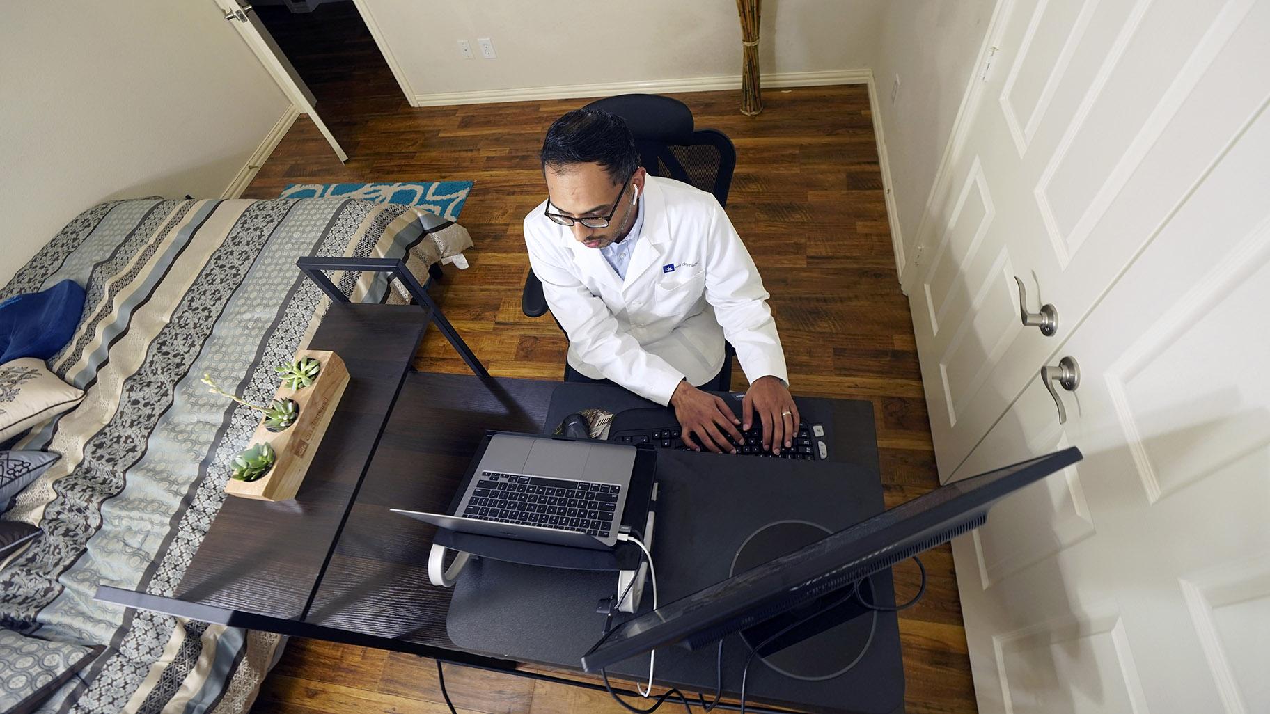 Medical director of Doctor on Demand Dr. Vibin Roy types notes as he listens to a patient during an online primary care visit from his home, Friday, April 23, 2021, in Keller, Texas. (AP Photo / LM Otero)
