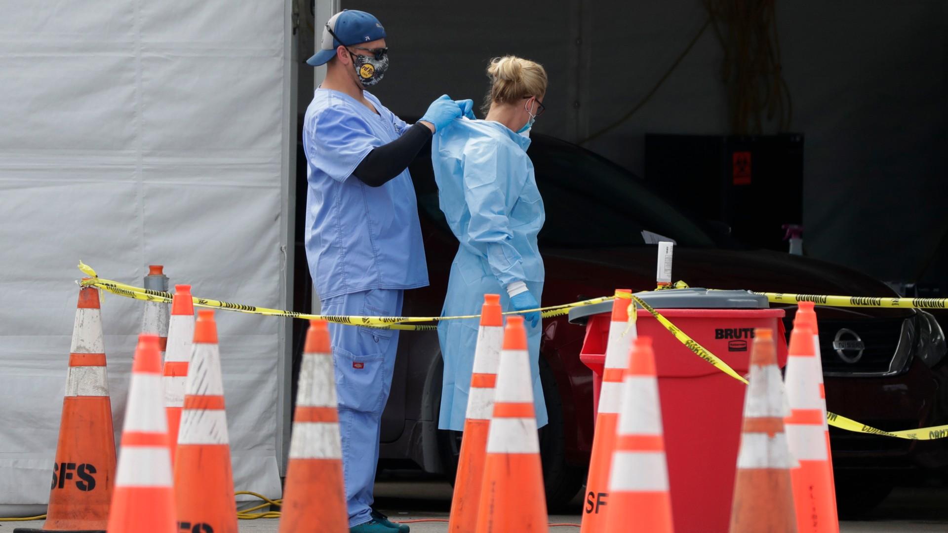 In this July 5, 2020, file photo, healthcare workers help each other with their personal protective equipment at a drive-thru coronavirus testing site outside Hard Rock Stadium in Miami Gardens, Fla. (AP Photo / Wilfredo Lee, File)
