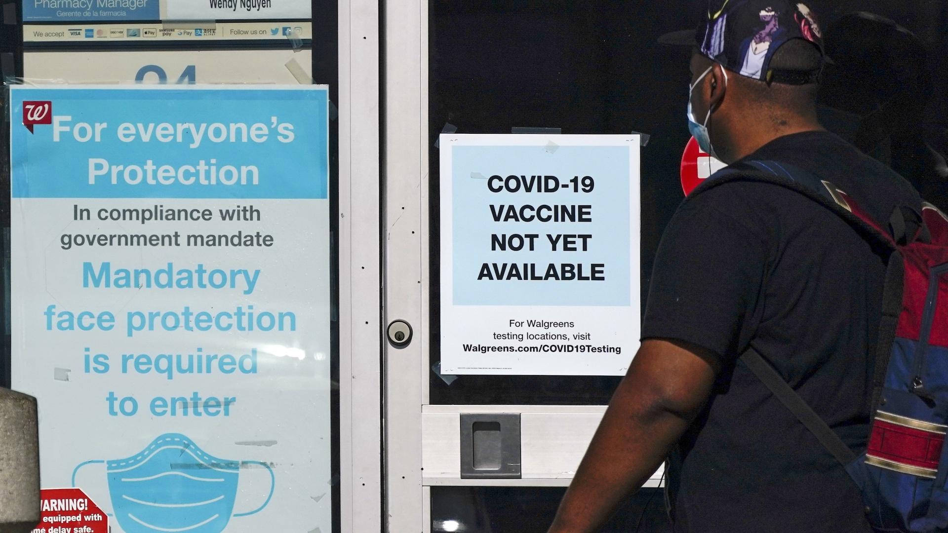 In this Dec. 2, 2020, file photo, a customer walks past a sign indicating that a COVID-19 vaccine is not yet available at Walgreens in Long Beach, Calif. (AP Photo/Ashley Landis)