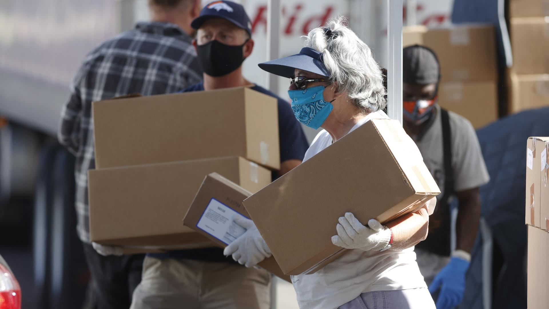 In this June 26, 2020, file photo, volunteers Juanita MacKenzie, front, and Dave Stutman carry boxes of food to a waiting car at a large mobile pantry set up by the Food Bank of the Rockies in the parking lot of Empower Field at Mile High in west Denver. (AP Photo/David Zalubowski, File)