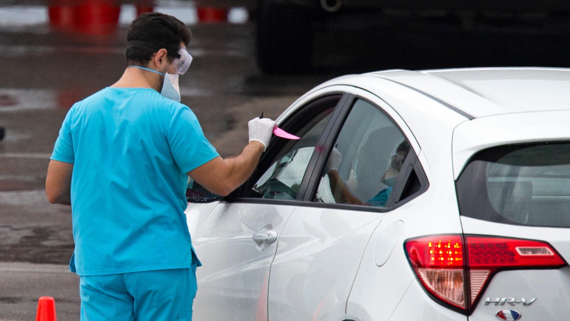 Vehicles line up as a health care worker helps to check in as citizens is being tested at the COVID-19 drive-thru testing center at Hard Rock Stadium in Miami Gardens on Sunday, November 22, 2020. (David Santiago / Miami Herald via AP)