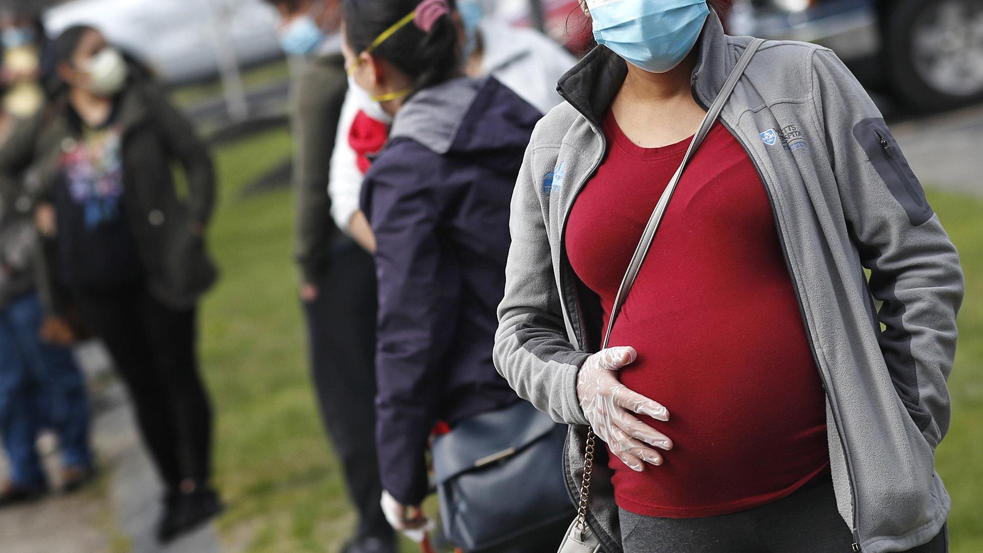 In this Thursday, May 7, 2020 file photo, a pregnant woman wearing a face mask and gloves holds her belly as she waits in line for groceries with hundreds during a food pantry sponsored by Healthy Waltham for those in need due to the COVID-19 virus outbreak, at St. Mary's Church in Waltham, Mass. (AP Photo / Charles Krupa)