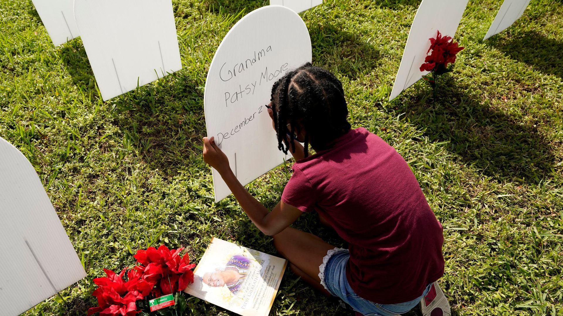 In this Nov. 24, 2020, file photo, Kyla Harris, 10, writes a tribute to her grandmother Patsy Gilreath Moore, who died at age 79 of COVID-19, at a symbolic cemetery created to remember and honor lives lost to COVID-19 in the Liberty City neighborhood of Miami. (AP Photo / Lynne Sladky, File)