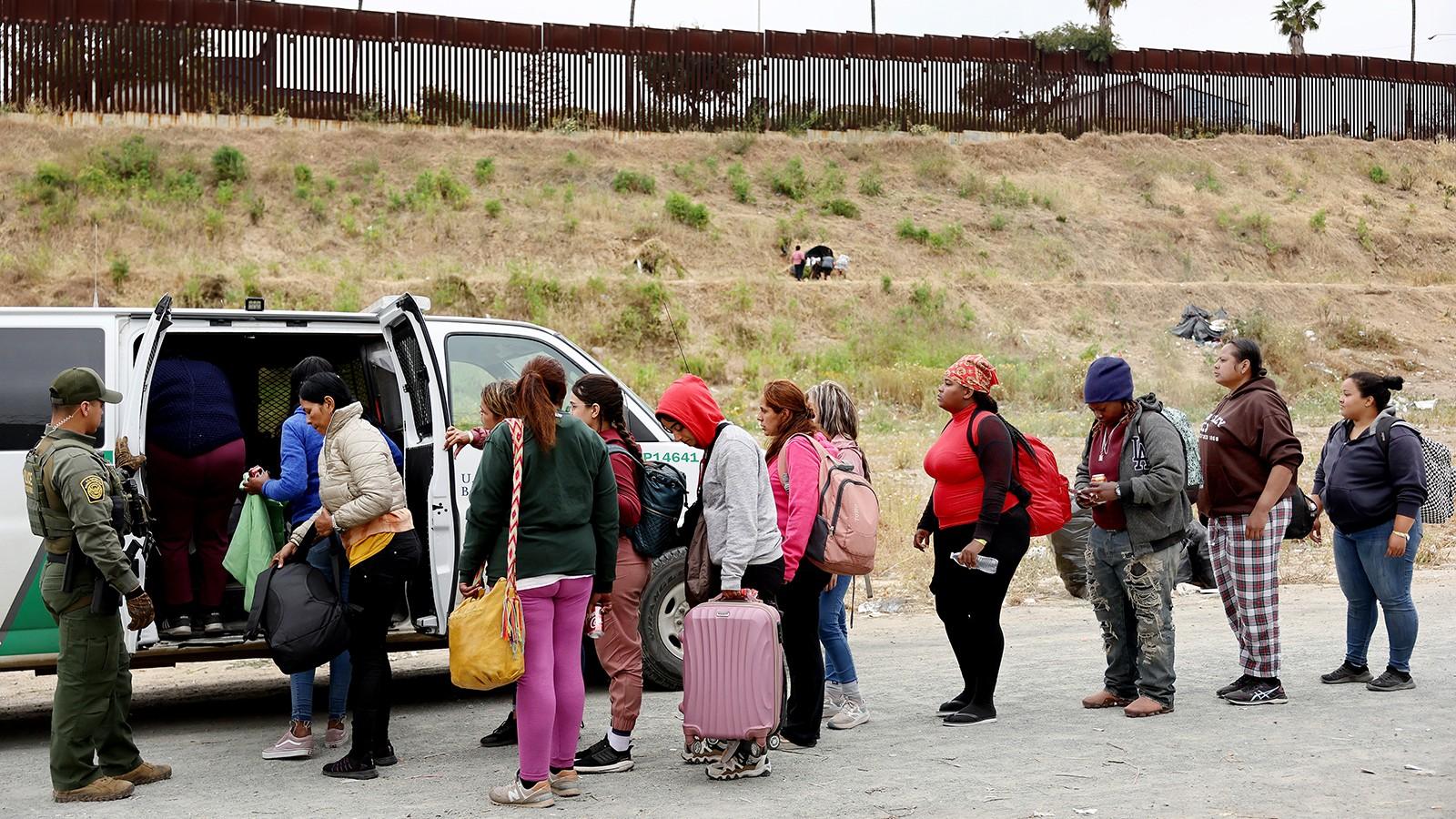 A Border Patrol agent keeps watch as immigrants enter a vehicle to be transported from a makeshift camp on May 13, 2023 in San Diego, California. (Maria Tama / Getty Images via CNN)