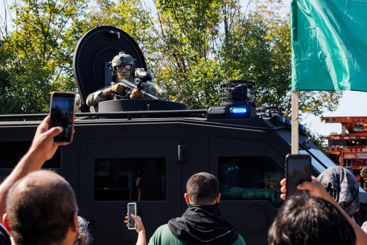 An ICE officer watches protestors as a Lenco BearCat vehicle drives to the scene in the Brighton Park neighborhood of Chicago, on Saturday, Oct. 4, 2025, after protesters learned that U.S. Border Patrol shot a woman Saturday morning on Chicago's Southwest Side. (Anthony Vazquez / Chicago Sun-Times via AP)