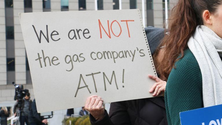 A demonstrator holds a sign reading, “We are NOT the gas company’s ATM!” at a Jan. 6, 2026, rally held by consumer, environmental and community activists. (Maggie Dougherty / Capitol News Illinois)