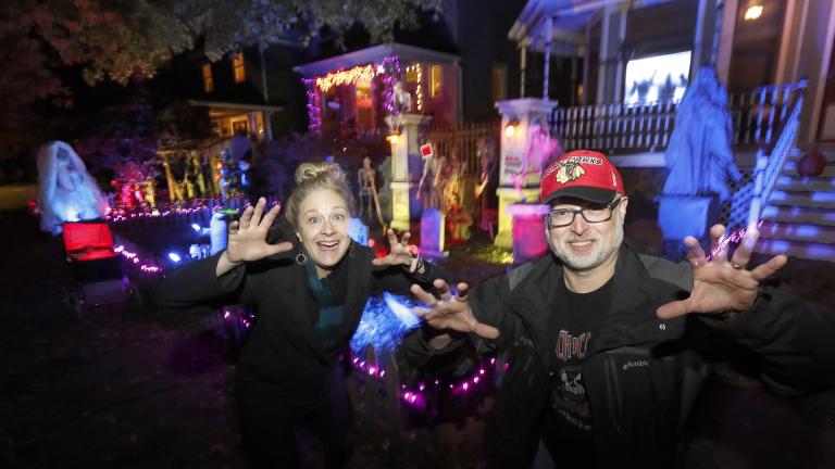In this Tuesday, Oct. 29, 2019 photo, neighbors Beth LeFauve, left, and Nelson Gonzalez pose for a portrait outside their two Bernard Street homes and the Halloween decorations spanning both properties in Chicago. (AP Photo / Charles Rex Arbogast)