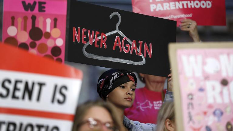 In this Tuesday, May 21, 2019 file photo, August Mulvihill, of Norwalk, Iowa, center, holds a sign depicting a wire clothes hanger during a rally at the Statehouse in Des Moines, Iowa, to protest recent abortion bans. (AP Photo / Charlie Neibergall)