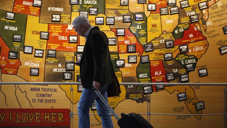 In this March 18, 2020 photo, a traveler checks his mobile telephone while passing a map of the United States on the way to the security checkpoint in the main terminal in Denver International Airport. (AP Photo / David Zalubowski)