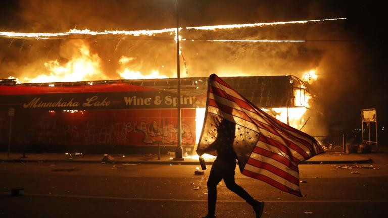 A protester carries a U.S. flag upside down, a sign of distress, next to a burning building Thursday, May 28, 2020, in Minneapolis. (AP Photo / Julio Cortez)