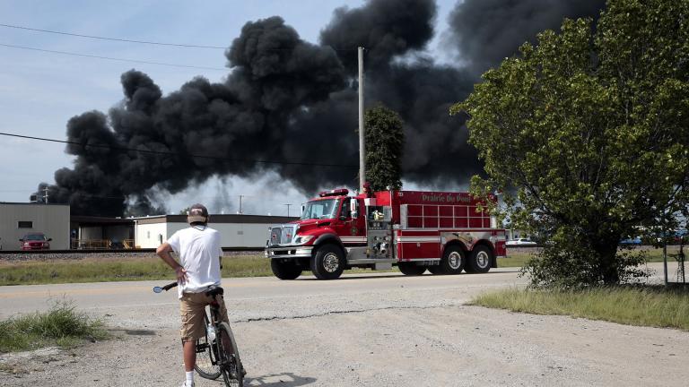 A resident watches as a fire truck arrives in downtown Dupo, Illinois, to help fight a tanker fire from a derailed train on Tuesday, Sept. 10. 2019. Black smoke coming from the derailment scene can be seen for miles and caused the evacuation of schools in the town, authorities said. (Robert Cohen / St. Louis Post-Dispatch via AP)