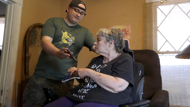 In this Tuesday, April 28, 2020, photo Zach Stafford, left, shows his mother, Debra Mize, a news alert on his phone as they watch a livestream of the daily coronavirus briefing by Illinois Gov. J.B. Pritzker on a television just out of view inside their home in Belleville, Illinois. (AP Photo / Jeff Roberson)