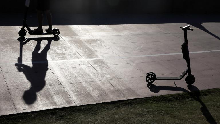 In this May 28, 2019, file photo, a man on a scooter passes a parked scooter along the Mission Beach boardwalk in San Diego. (AP Photo / Gregory Bull, File)