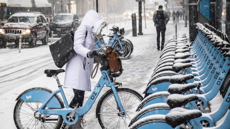 A woman clears off a Divvy bike as a winter weather advisory is issued for the Chicago area on Monday, Nov. 11, 2019, in Chicago. (Rich Hein / Chicago Sun-Times via AP)