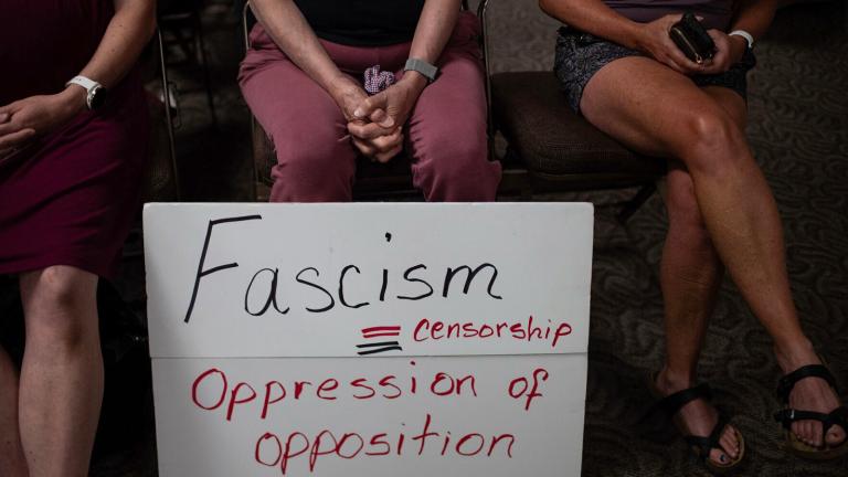 Three people sit with a sign at a Campbell County, Wyo., Library Board meeting, July 23, 2023, in Gillette, Wyo. (Ed Glazar / Gillette News Record via AP)