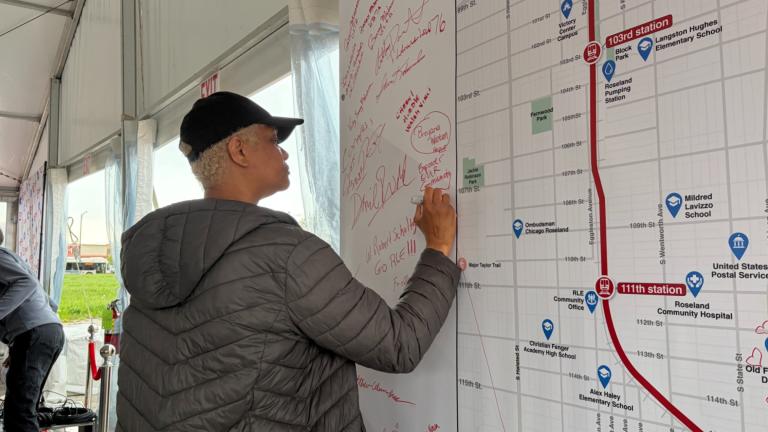 An attendee signs a poster during a Red Line extension project ceremonial groundbreaking event on April, 24, 2026, near Michigan Avenue and 116th Street, the future site of one of the new Red Line stations. (Eunice Alpasan / WTTW News)
