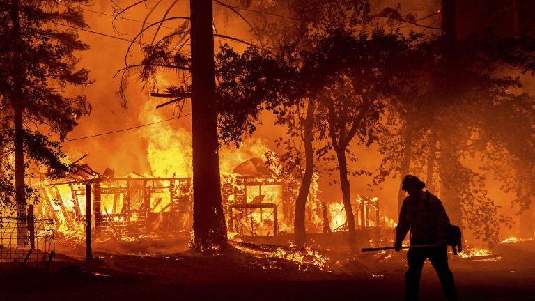 In this Saturday, July 24, 2021, file photo a firefighter passes a burning home as the Dixie Fire flares in Plumas County, Calif. (AP Photo / Noah Berge, File)